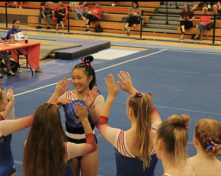 Bruins gymnast smiling and high-fiving teammates after her floor routine